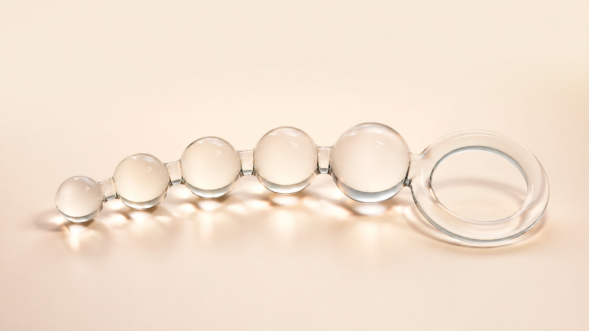 Clear progressive glass anal beads with a wide retrieval ring on a neutral background