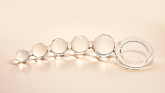 Clear progressive glass anal beads with a wide retrieval ring on a neutral background