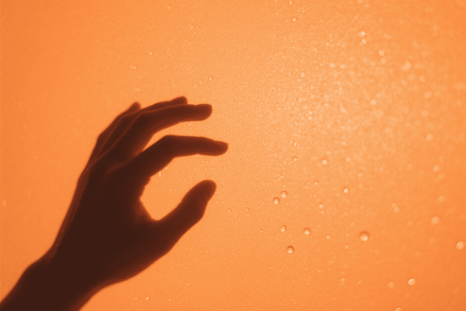 Silhouette of a hand making a circle gesture against an orange background